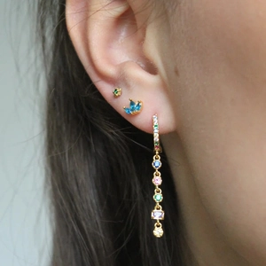 Macro shot of colorful zircon tassel earrings and gold studs on a model ear