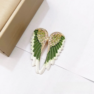 Close-up of green enamel angel wing brooch with sparkling rhinestones and gold plating