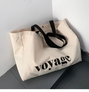 Macro detail of large canvas tote bag with black handles and voyage text embroidery