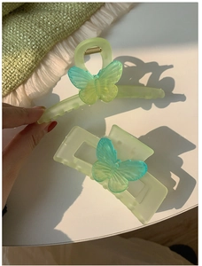 Macro detail of matte green hair clips featuring translucent gradient butterfly accents