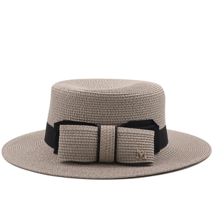 Flat top straw boater hat with black ribbon, bow, and gold M metal detail for beach