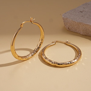 Detail of gold geometric hoop earrings with hammered texture on a neutral stone background