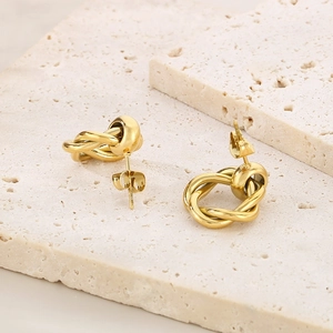 Polished gold double hoop knot earrings displayed on elegant beige travertine stone