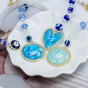 Blue heart evil eye pendant necklace with gold frame on white shell tray