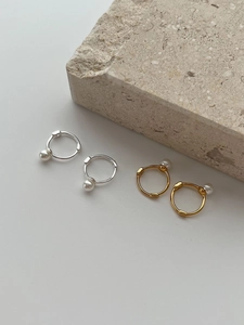 Detailed view of silver and gold pearl hoop earrings on a natural stone background