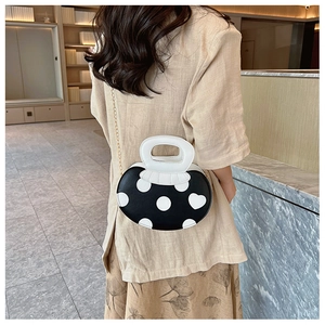 Detail of creative black cross-body bag with white polka dots and metal chain strap