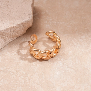 Detail of chunky gold chain ring featuring a polished metallic texture on a stone surface