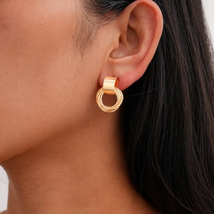 Close-up of elegant gold U-shaped earrings with textured rings worn by a model