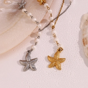 Macro shot of silver and gold starfish pendants with pearls on wet background