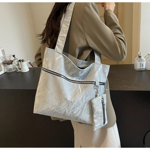 Detail of silver tote bag with crinkled texture and side pouch in a cafe setting