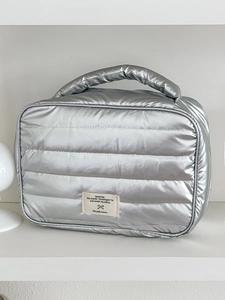 Detailed view of silver puffer makeup bag featuring horizontal quilting and woven label