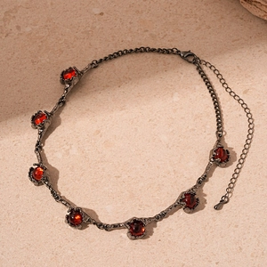 Macro shot of gothic necklace with rough dark metal texture and six red round gemstones