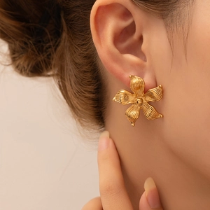 Close-up of golden flower stud earrings with a textured petal design on a model
