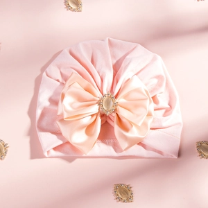Detail of baby pink turban hat featuring a large satin bow and central gemstone accent