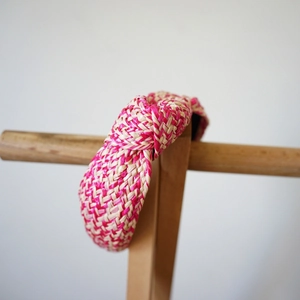 Detail of fuchsia and beige woven raffia headband with top knot on a wooden stand