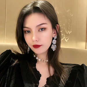 Detail of luxury teardrop crystal earrings and pearl choker with gold emblem on a model