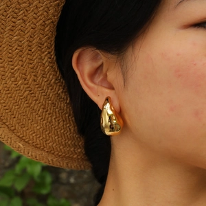 Golden irregular teardrop earrings with a polished finish worn by a model in a summer setting