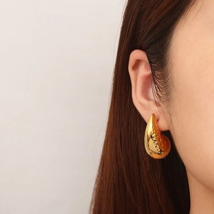Detail of gold water drop earring with hammered texture worn on ear for women