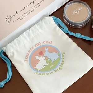 Close-up of white canvas drawstring bag with cute rabbit print and heart pattern on wood
