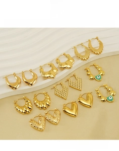 Detailed set of gold titanium steel earrings with heart and eye motifs on white stands