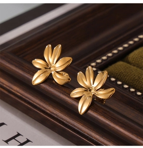 Detailed macro view of gold-plated five-petal flower stud earrings on a wooden prop