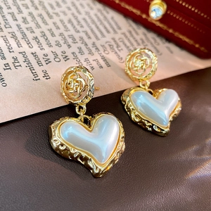 Macro shot of gold hollow flower earrings with white pearl heart pendants in a jewelry box