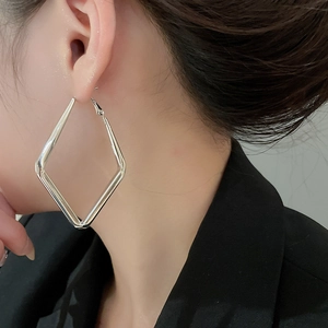 Close-up of model wearing silver geometric diamond hoop earrings with polished finish