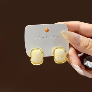 Detail of rectangular marble textured earrings with a gold frame held in hand