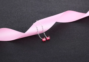 Detail of red zircon drop earrings hanging on a pink ribbon against a black background