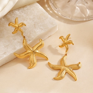 Golden double starfish drop earrings with textured finish on a seaside themed background