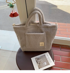 Detail of light gray faux shearling tote bag with a front pocket on a leather stool