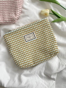 Macro detail of checkered knit makeup bag featuring woven texture and white logo label