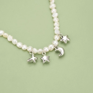 Baroque pearl necklace with silver star and moon charms over a soft green background