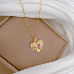 Macro shot of gold necklace with pink heart winged pendant on a silk background
