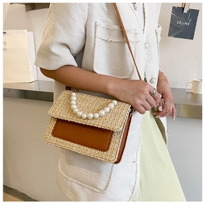 Detail of straw woven bag featuring a brown leather patch and elegant large pearl handle