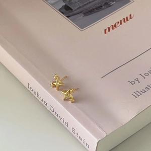 Minimalist 925 sterling silver star stud earrings in gold finish on a decorative book