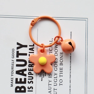Detailed view of orange knitted flower keychain with matching bell on a white card