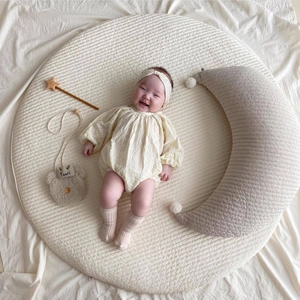 Cotton nursing pillow and newborn jumpsuit set on a quilted round moon play mat
