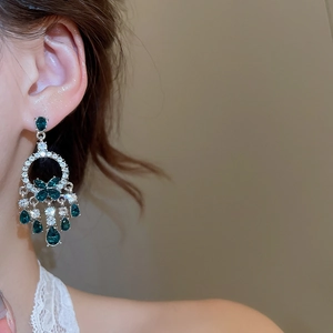 Dettaglio di orecchini a goccia in argento con strass verdi e bianchi indossati da una modella