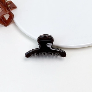 Close-up of a small dark brown jelly hair claw clip with a glossy finish on a white tray