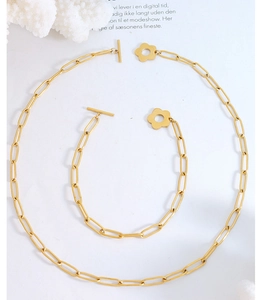 Macro detail of gold paperclip chain jewelry set featuring a floral toggle clasp