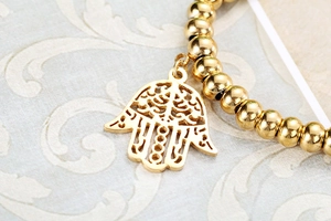 Macro detail of gold beaded stretch bracelet featuring a cutout Hamsa Hand charm