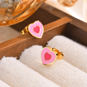 Close-up of heart earrings in gold finish with pink and red enamel on white velvet