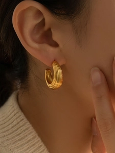 Gros plan d'une boucle d'oreille créole en C dorée avec texture rayée sur l'oreille du modèle