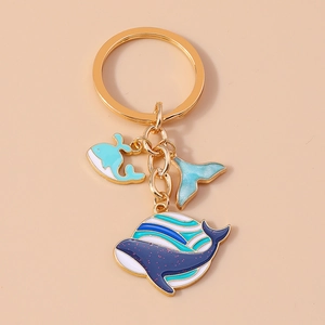 Détail d'un porte-clés baleine avec anneau doré et trois charms émaillés aux tons bleus
