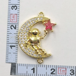 Close-up of gold moon and astronaut necklace measured with rulers on white surface