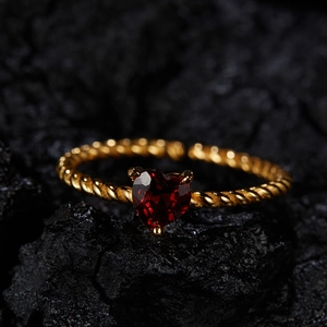 Macro shot of twisted gold band ring with heart-shaped red garnet stone on dark rock