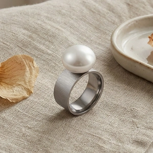 Detail of wide brushed silver stainless steel ring with a large white pearl on beige linen