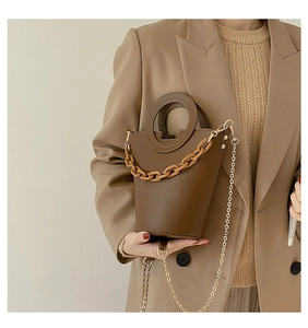 Detail of a brown leather bucket bag featuring a resin chain and hollow round handle