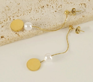 Detail of long gold snake chain pearl earrings featuring a polished round pendant